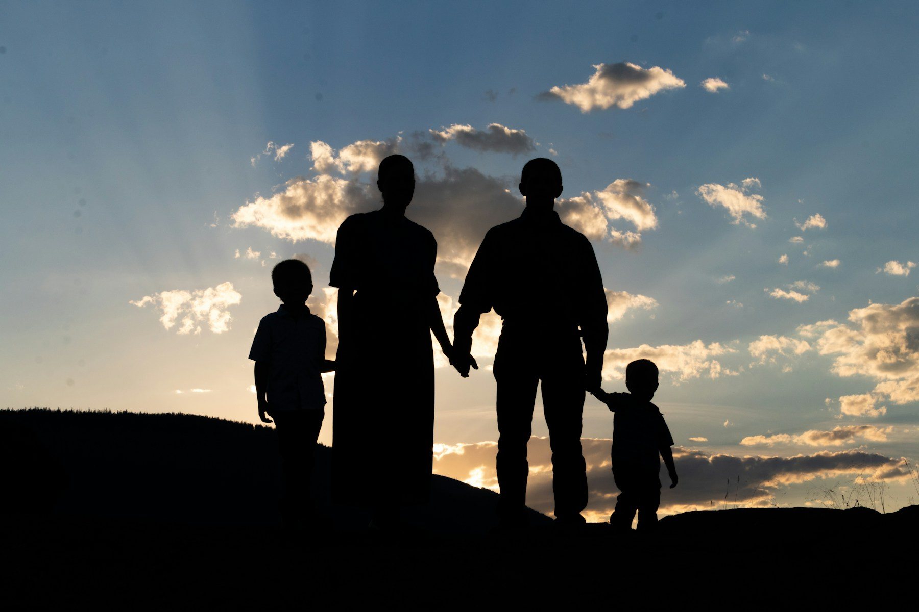 Family of four holding hands in silhouette against a sunset sky